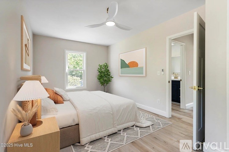 A bedroom with a bed, a lamp, a plant, and a painting on the wall.