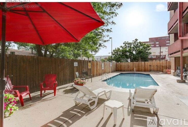 A pool area with a red umbrella and chairs.