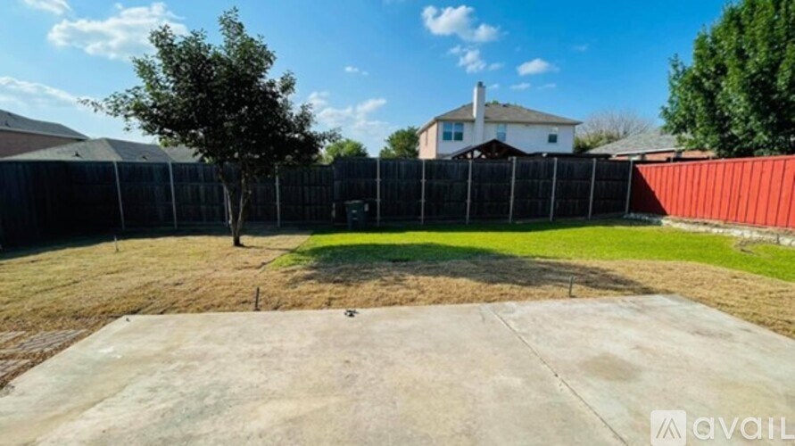 A backyard with a fence, a tree, and a house in the background.
