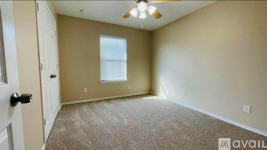 A room with beige walls and carpeted floor with a ceiling fan.