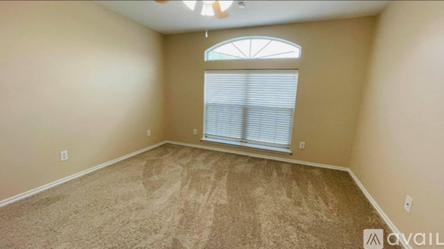 A room with beige walls and carpeting, a window with blinds, and a chandelier.
