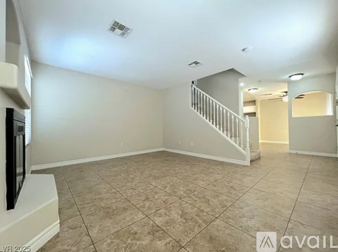 A spacious room with a tiled floor and a staircase in the background.