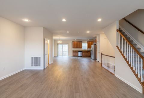 A spacious living room with hardwood floors and a staircase on the right side.