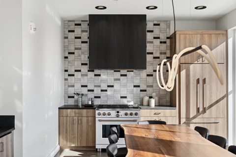 A modern kitchen with a wooden table and black and white tiles on the wall.