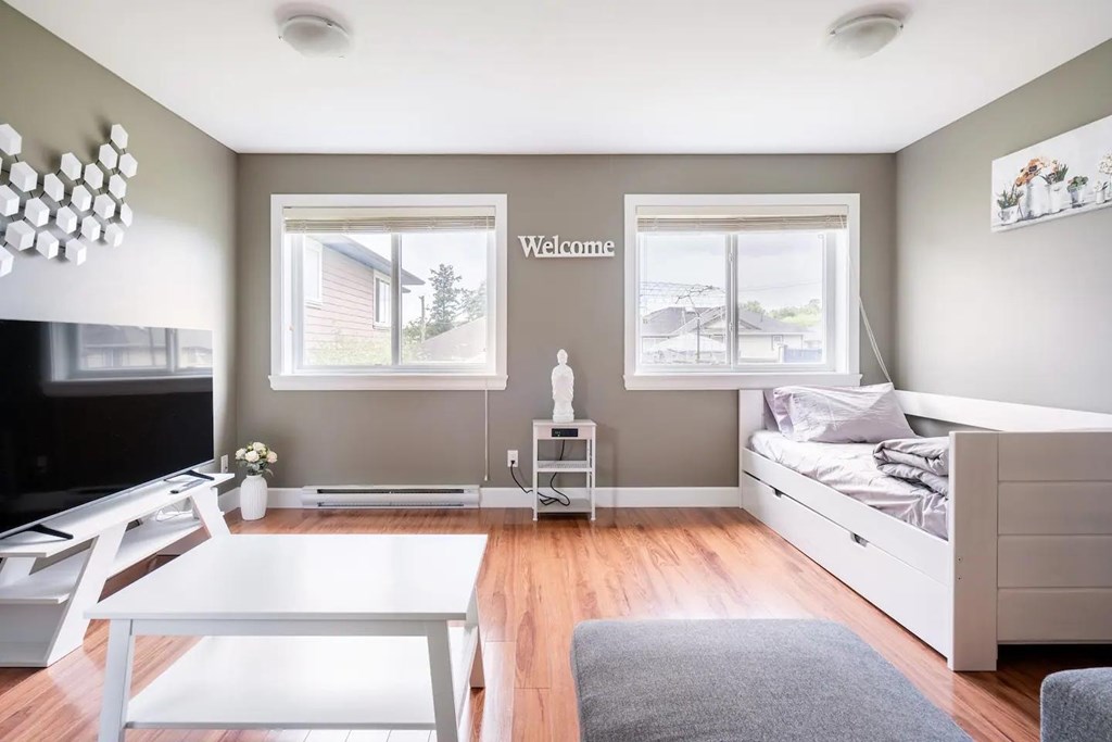 A bedroom with a bed, a table, and a window with a "Welcome" sign on the wall.