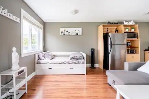 A modern living room with a white sofa and a bed with a grey blanket.