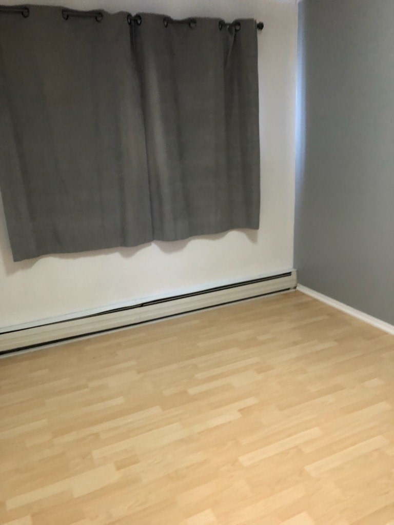 A grey curtain hangs on a white wall above a wooden floor.