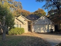 A house with a grey roof and a brown wall is surrounded by trees.