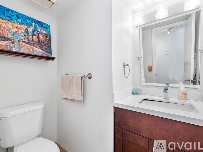 A bathroom with a toilet, a sink, and a painting on the wall.