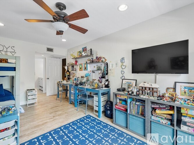 A room with a ceiling fan and a flat screen TV mounted on the wall.