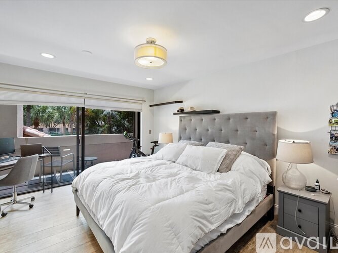 A bedroom with a large bed, a desk with a chair, and a balcony with a view of trees.