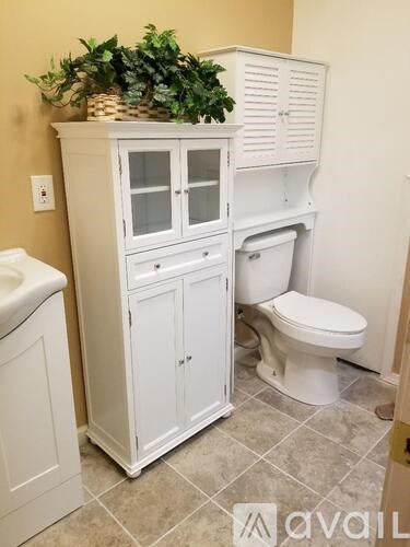A white cabinet with glass doors is in a bathroom with a toilet.