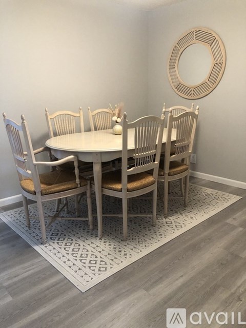 A dining room with a round mirror and a white table with chairs around it.