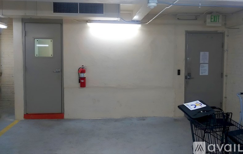 A room with a grey door, a red fire extinguisher and a black table.