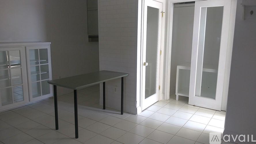 A table with a black top and black legs is in the middle of a room with white walls and a white tiled floor.