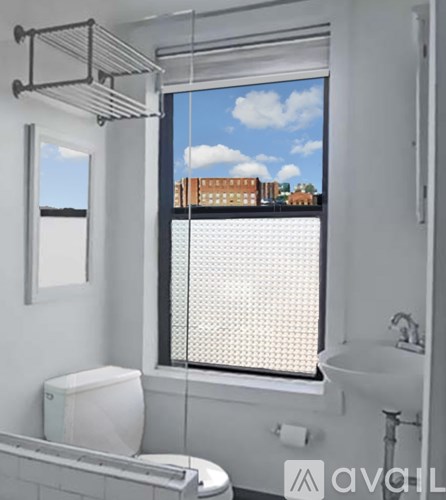 A bathroom with a toilet, sink, and window with a view of a cityscape.
