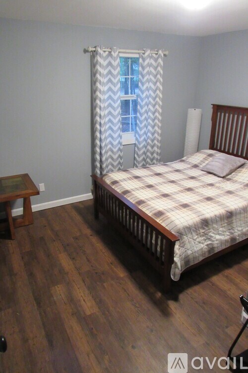 A bedroom with a bed, wooden headboard, and a window with a blue and white curtain.