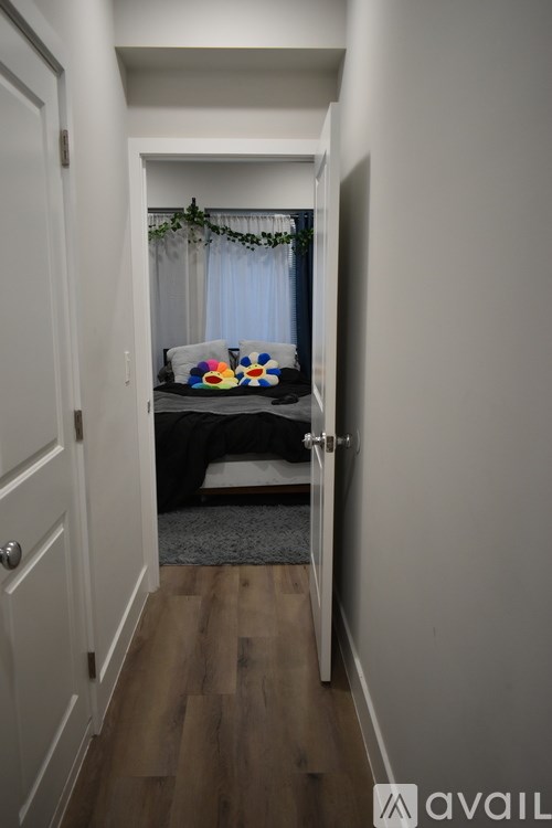 A hallway with a door on the left and a bedroom with a bed and a window on the right.