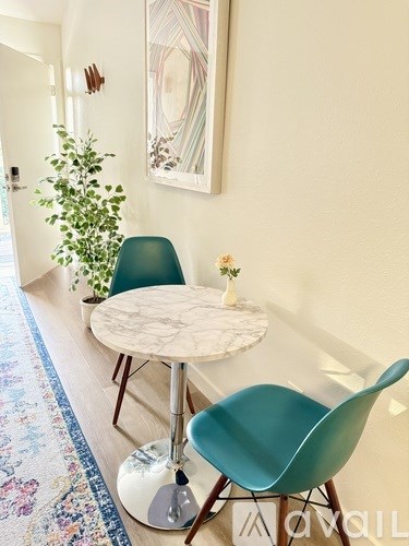 A white table with a green chair in front of a white wall with a painting hanging on it.