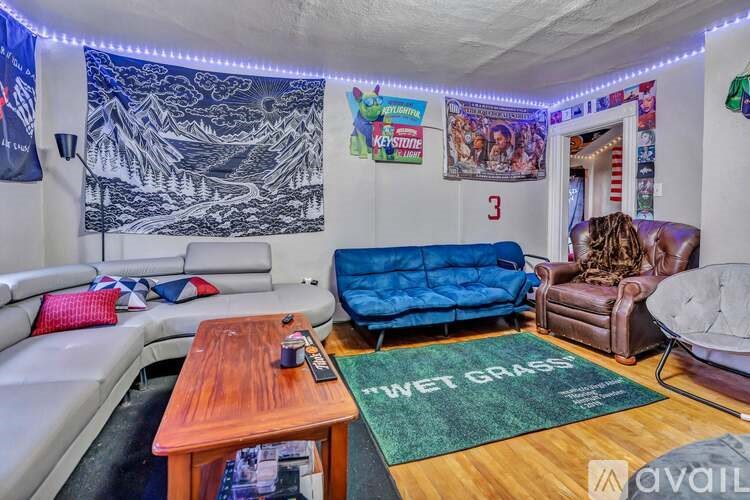A living room with a couch, a chair, a coffee table, and a rug with the text "WET GRASS" on it.