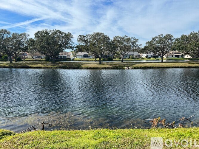 A serene lake surrounded by lush greenery and residential houses in the distance.