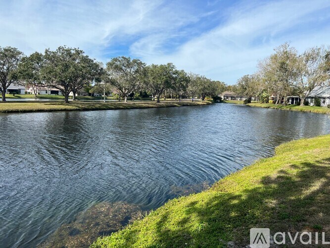 A calm lake surrounded by trees and houses under a clear blue sky.
