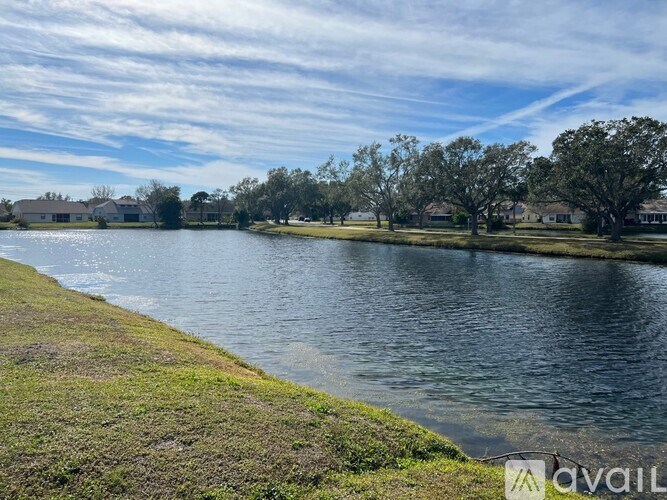 A body of water surrounded by grass and trees under a blue sky.