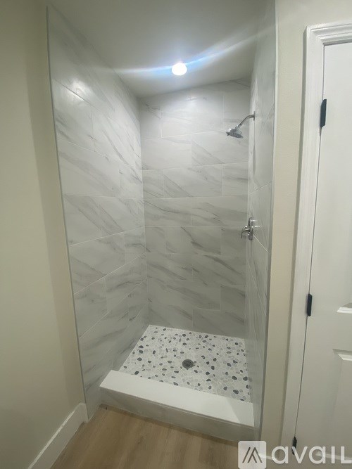 A white tiled shower with a shower head and a drain.
