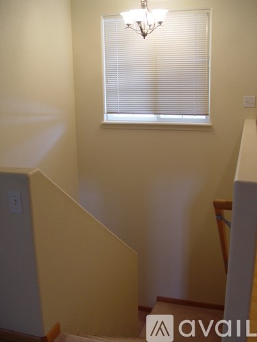 A chandelier hangs over a window with blinds in a room with a staircase.