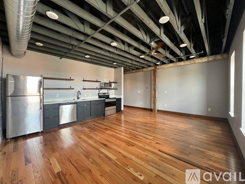 A spacious room with wooden floors and a kitchen area with stainless steel appliances.