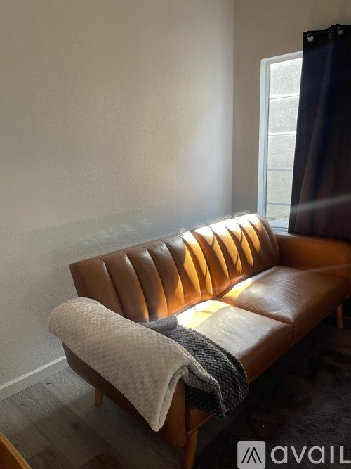 A brown leather couch with a grey blanket on it.