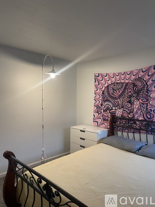 A bedroom with a bed, a wall hanging, and a lamp.