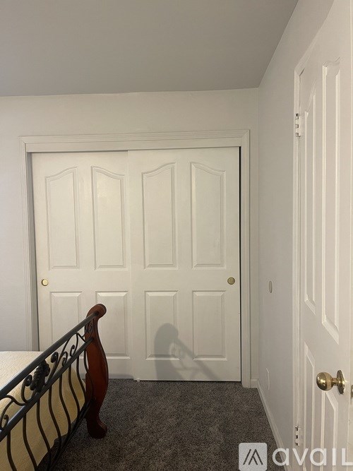 A white door with a gold handle is in a room with a black railing.