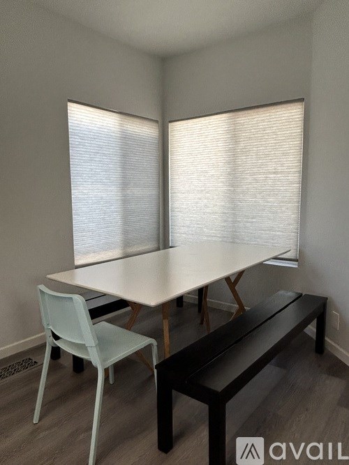 A white table with a white chair and a black bench in front of a window with blinds.