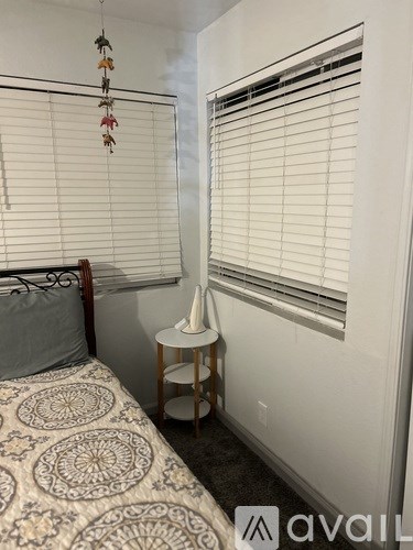 A bedroom with a bed, a small table with a lamp, and a window with blinds.