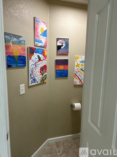 A hallway with four paintings on the wall and a roll of toilet paper.