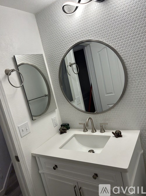 A white bathroom sink with a round mirror above it.