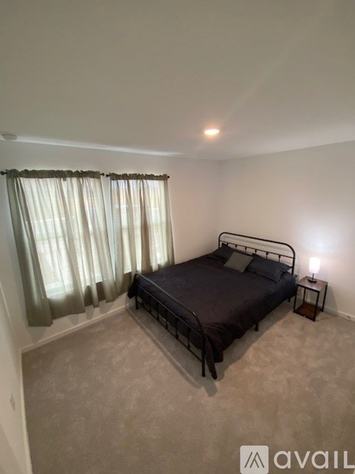 A bedroom with a bed, nightstand, and window with curtains.