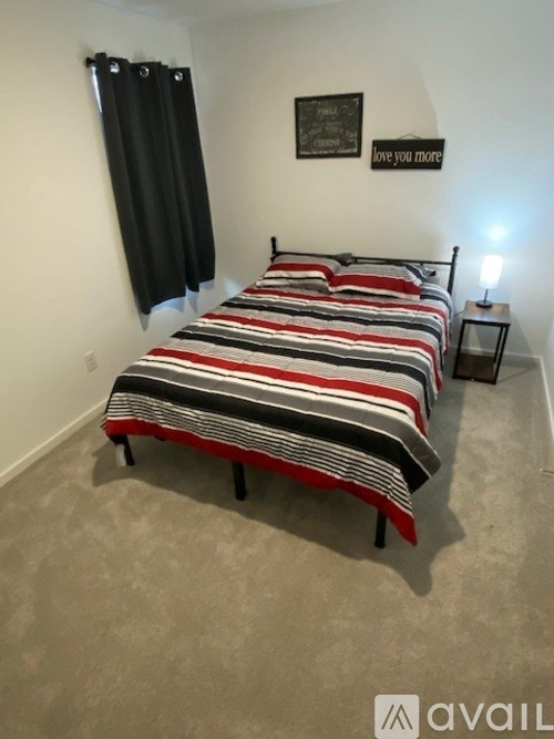 A bed with a striped comforter is in a room with a sign that says "love you more".