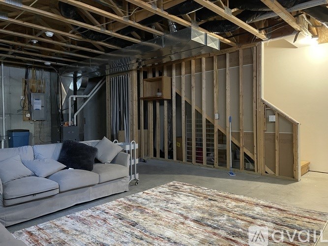 A living room with a grey couch and a rug in the foreground and a staircase in the background.