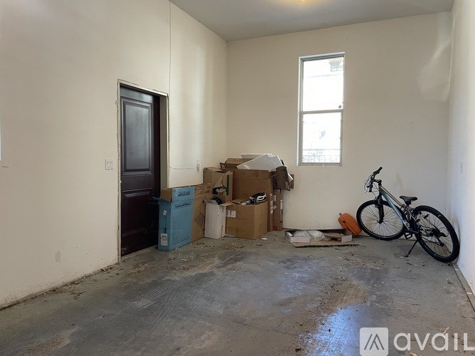 A room with a bicycle, a door, and a window with boxes and other items scattered around.