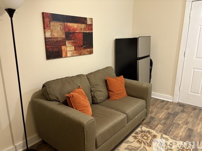 A brown couch with two pillows sits in a room with a black fridge and a painting on the wall.