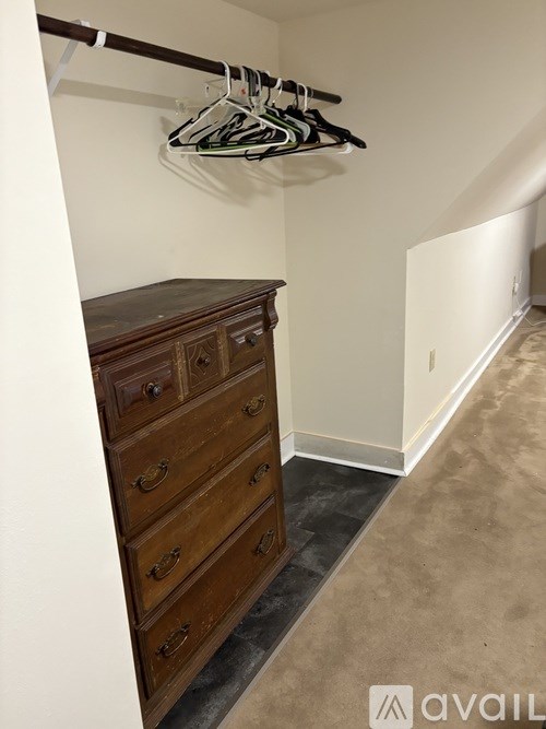A wooden chest of drawers in a room with a hanging clothes rack.