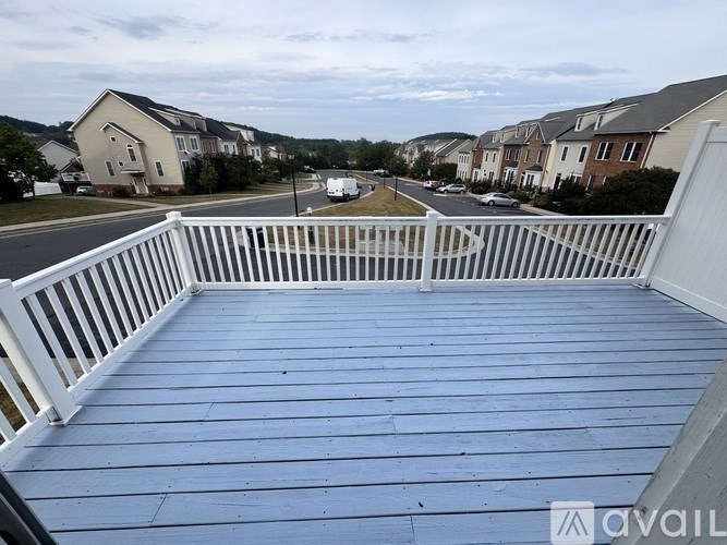 A white deck with a railing overlooking a street with houses and cars.