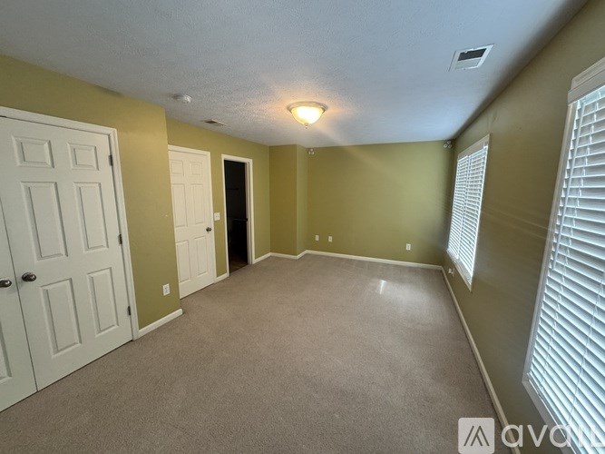 A room with a carpeted floor, a door, and a window with blinds.