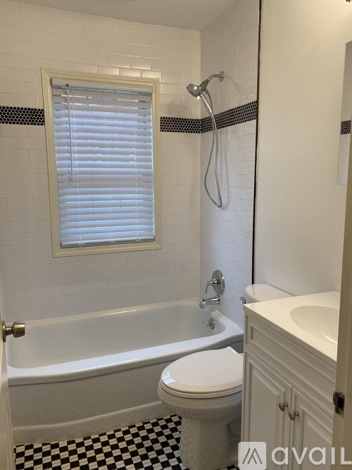 A white toilet sits next to a bathtub in a bathroom with black and white tiles.