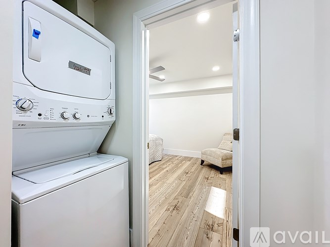 A white dryer and washer are in a small room with a door open to a living room.
