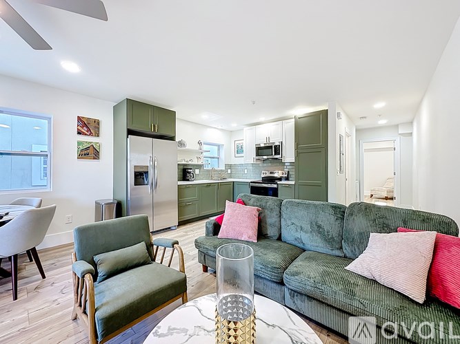A living room with a green couch and a glass table with a vase on it.