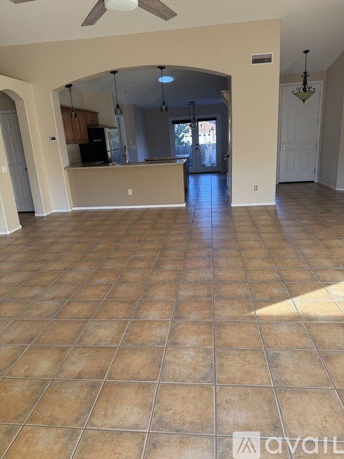 A spacious living room with a kitchen in the background and a fan on the ceiling.