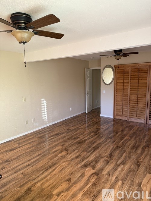 A room with wooden flooring and two ceiling fans.